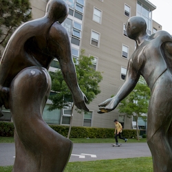 Statue on campus of two people almost touching hands